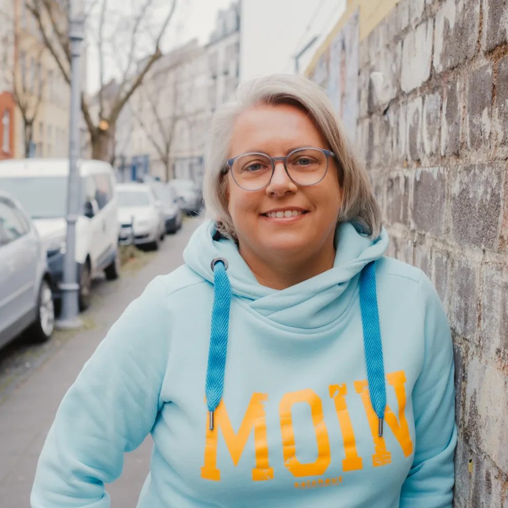 Kirsten Biema lächelnd im hellblauen MOIN-Hoodie