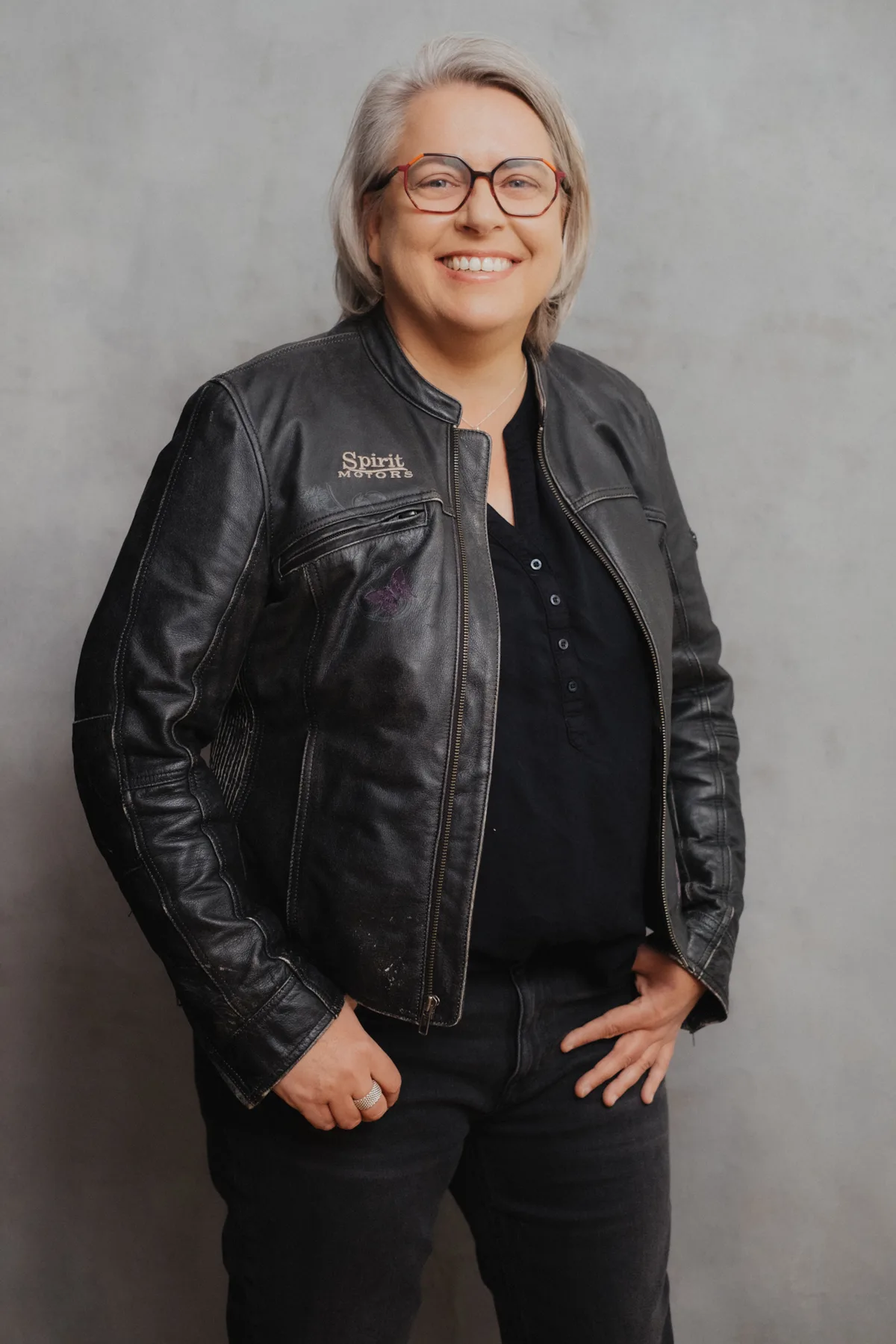 Kirsten Biema im Studio-Portrait, lächelnd in schwarzer Lederjacke